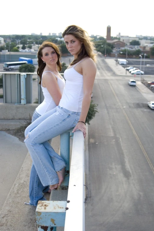 two beautiful young women standing on the side of a bridge