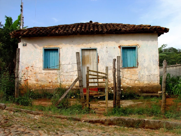 an old dilapidated building with blue shutters sits alone on the side of a street