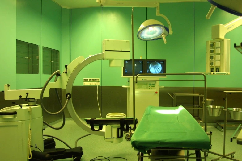 a green operating room has a monitor and chairs