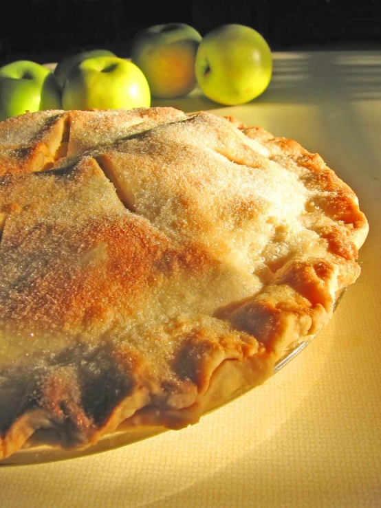 an apple pie on a plate with three apples in the background