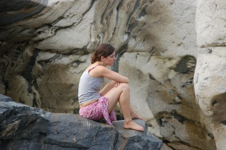 a young woman sits on a rock looking away