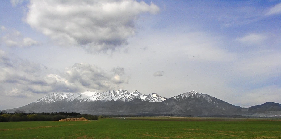 some grass white clouds and mountains and trees