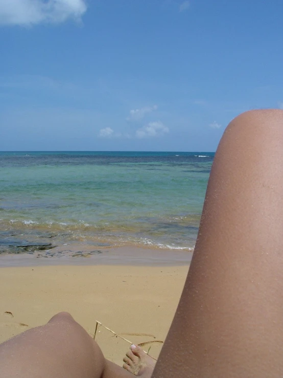 a beach with a person's legs facing the ocean