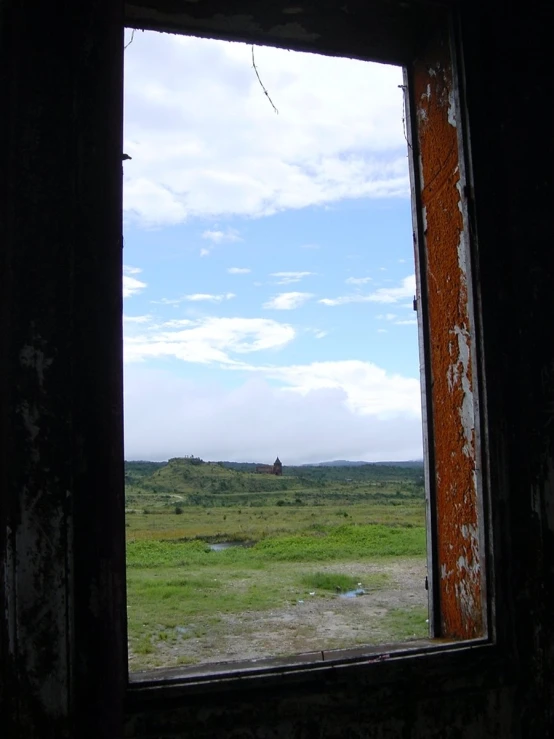 the view out an old window shows a grassy plain