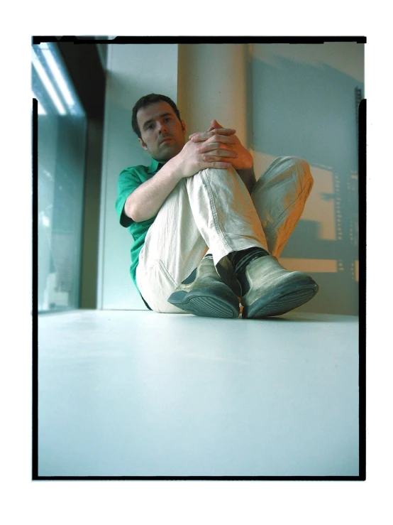 a man sits against a wall with his foot propped up in the corner