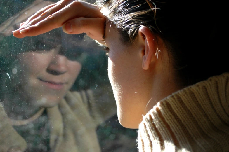 a young woman looks at the reflection of another person