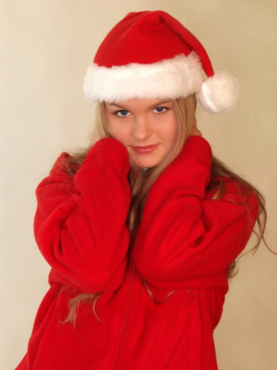 a young woman in a red santa hat smiles and waves her hand