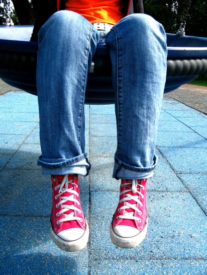 a person sitting on a bench wearing red converse sneakers