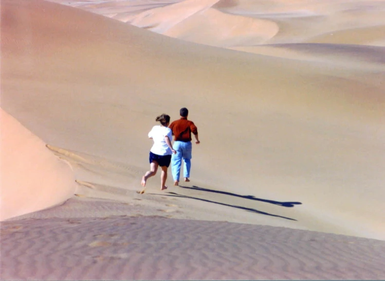 two people run through the desert with a snowboard