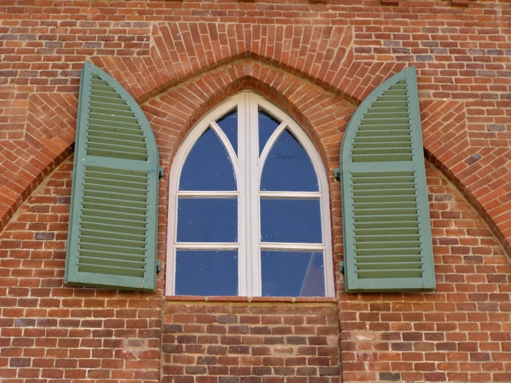 a brick wall with two open windows and shutters