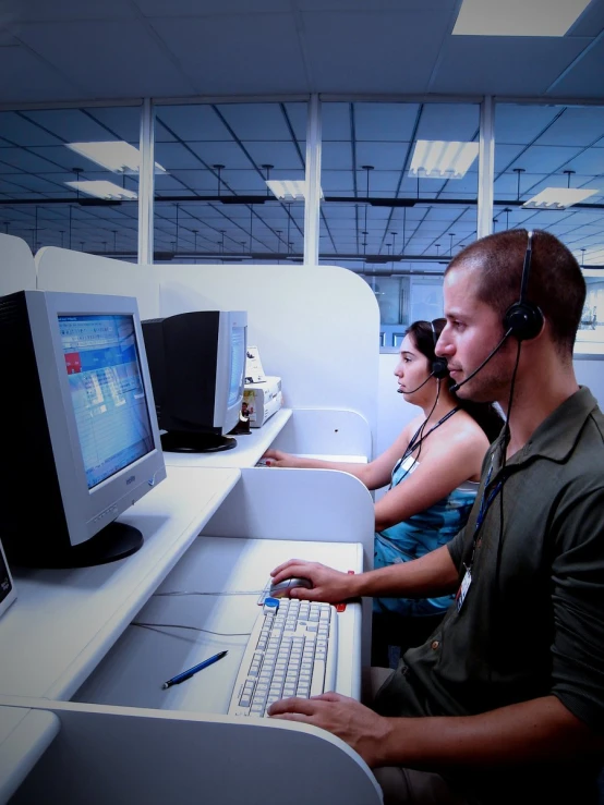 man and woman wearing headsets sitting in front of a computer monitor