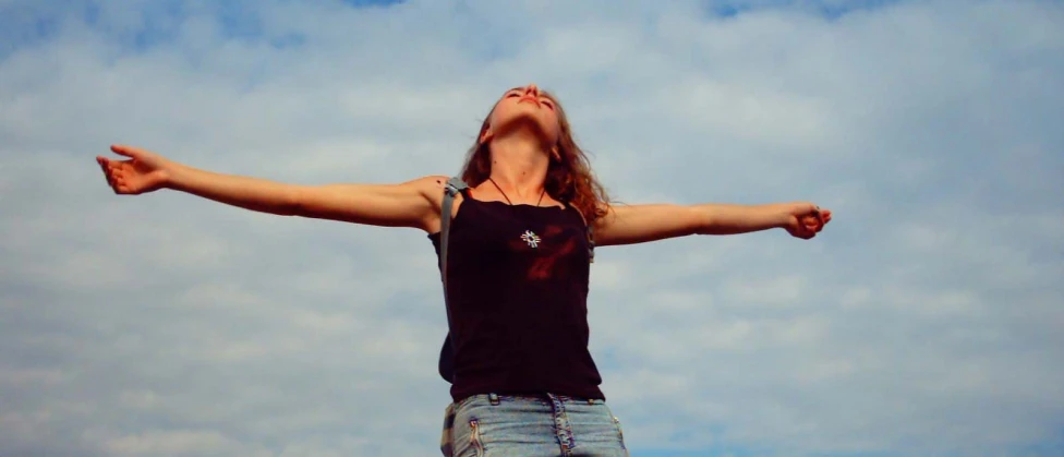 girl in jeans and tank top holding open arms with one leg in the air