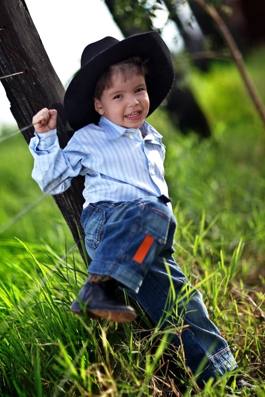 a  in jeans and a cowboy hat is leaning on a tree