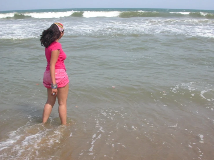 a young lady standing in the ocean water on a sandy beach