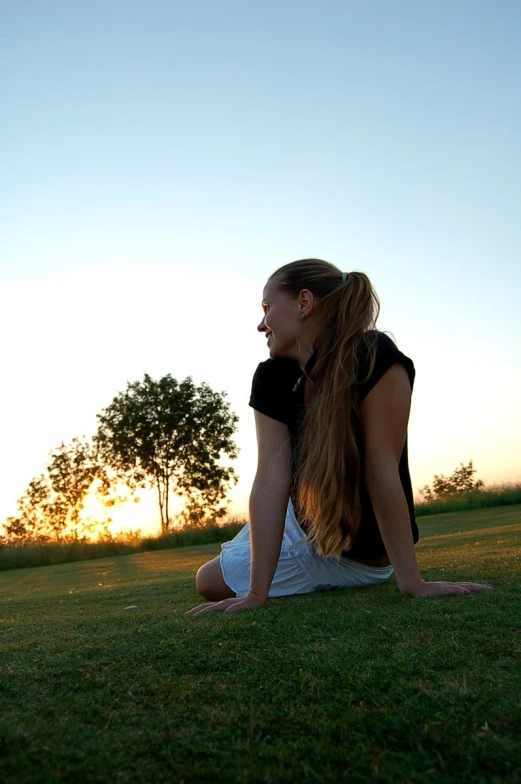 the girl is sitting in the grass staring into the distance