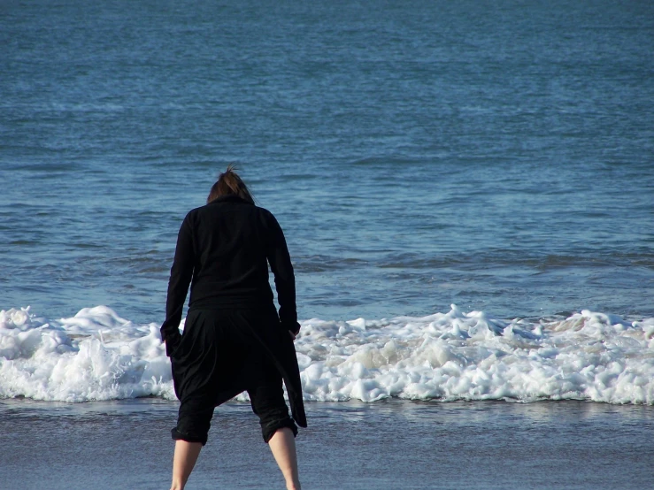 a woman walks along the beach and looks at the waves