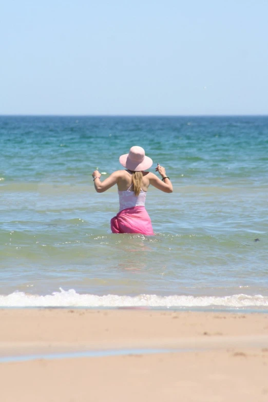 the woman with her arms raised wades through the water