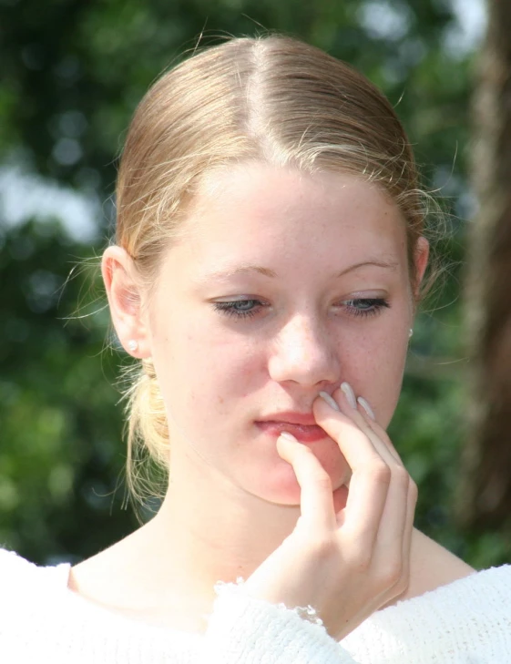 a girl is standing in front of a tree smoking a cigarette