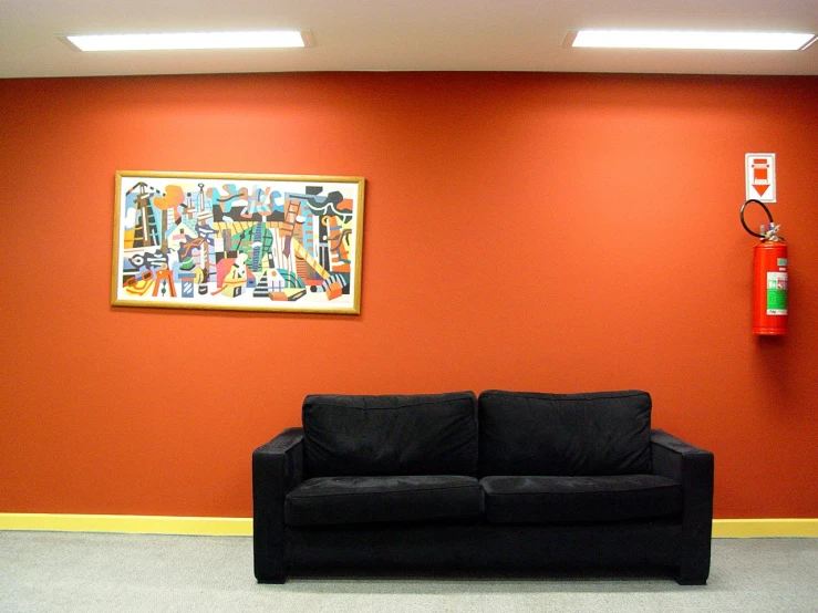 a couch sitting in front of a red wall next to a wall mounted phone