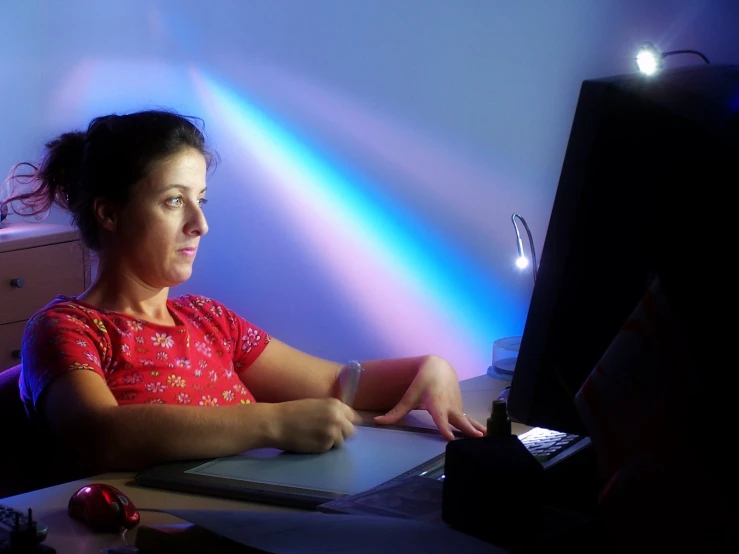 the woman sits at her computer in the spotlight