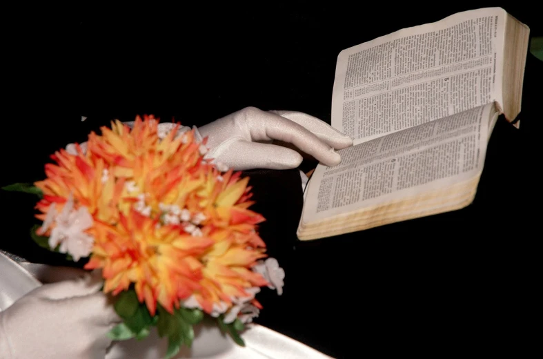 hand holding open book over decorated orange and white flower