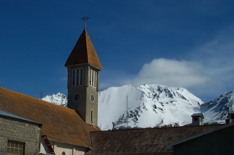 a church steeple stands in front of a snowy mountain