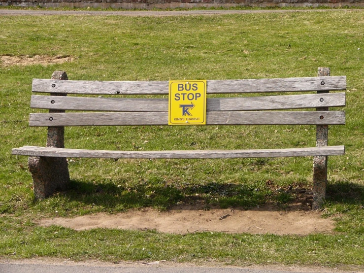 a park bench is in the grass, with a bus sign on it