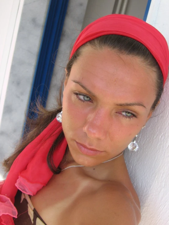 the woman is posing in front of a building wearing a red head scarf