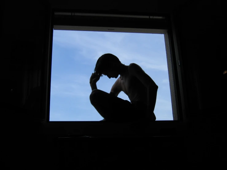 the silhouette of a man sits in front of a window