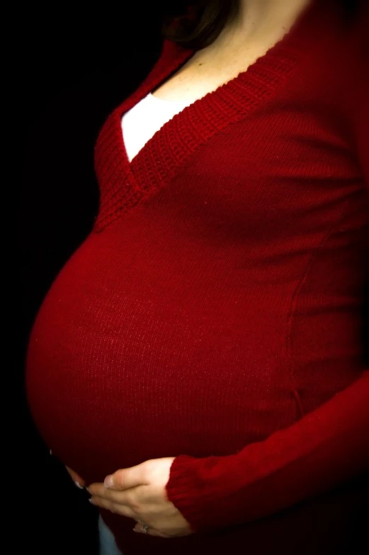 pregnant woman wearing a red sweater, dark background