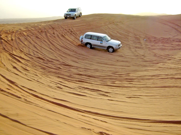 two cars are driving in a sandy dune