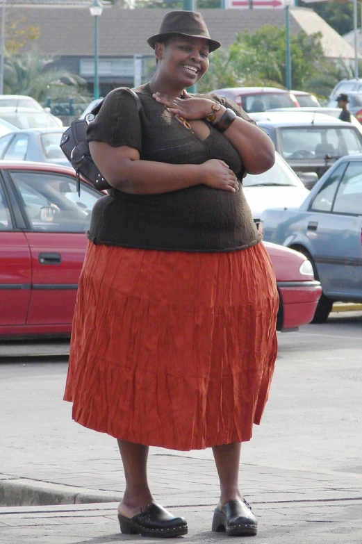 a woman in a skirt and shirt stands in a parking lot
