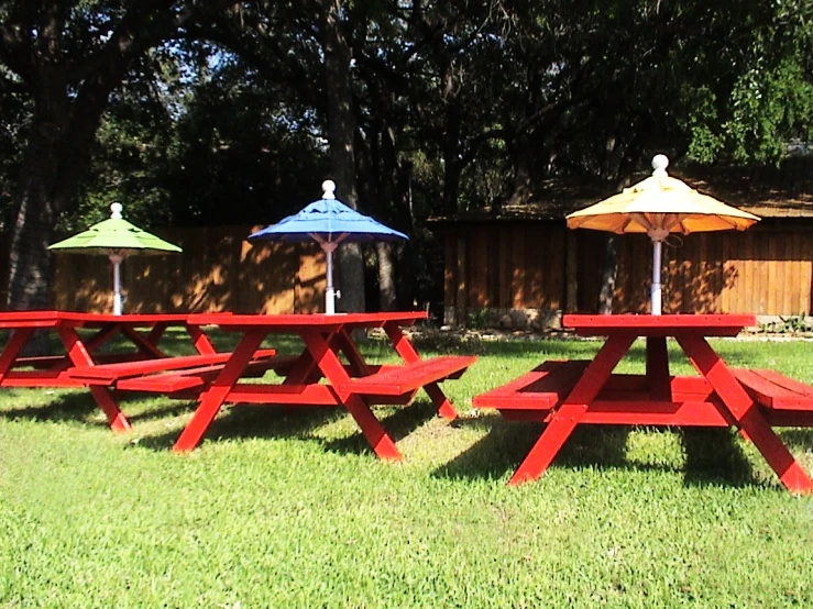 two red picnic tables and three multi colored umbrellas on grass