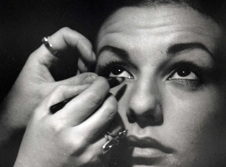 a black and white pograph of a lady fixing her makeup