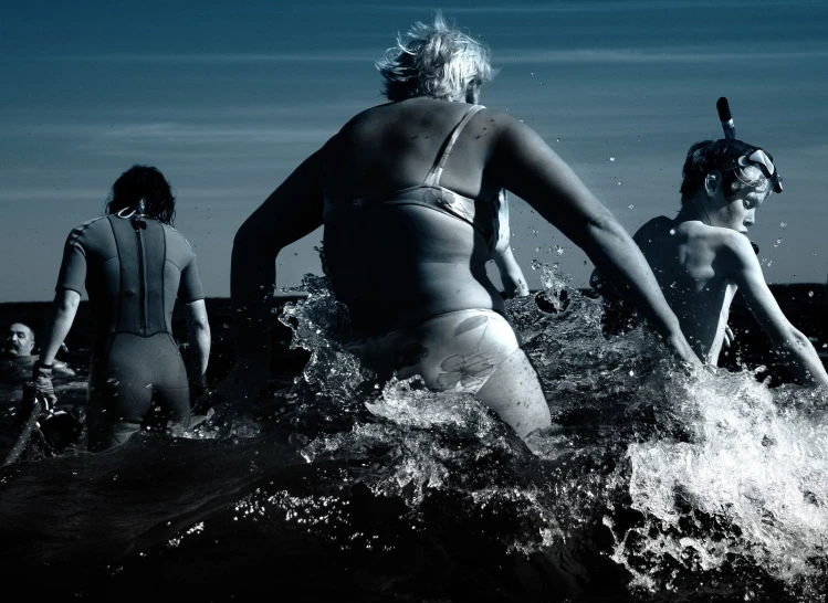 three women and one man standing in the ocean while another woman walks into the ocean