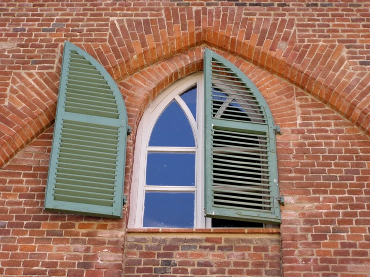 a window with two green shutters in front of a red brick wall