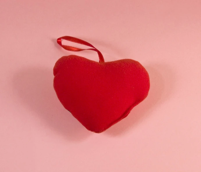 a red heart sitting on top of a pink surface