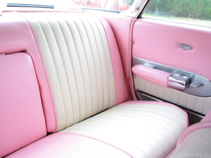 a pink car with white seats next to a car door