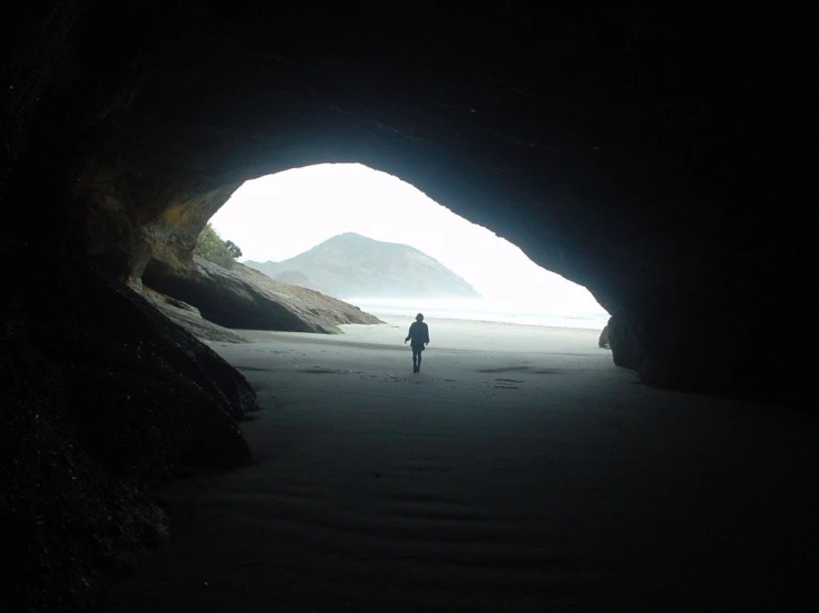 a person walking on a beach in front of an open cave