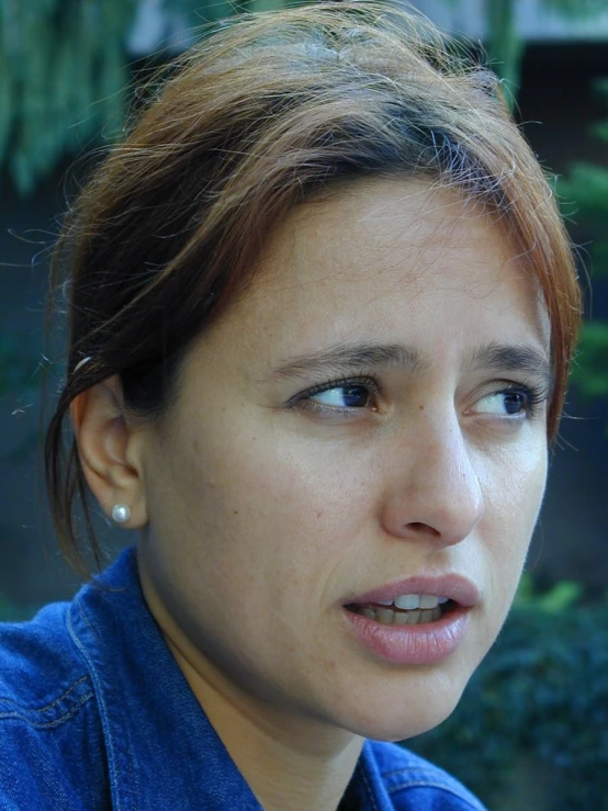 a woman in blue shirt looking ahead with green trees in background