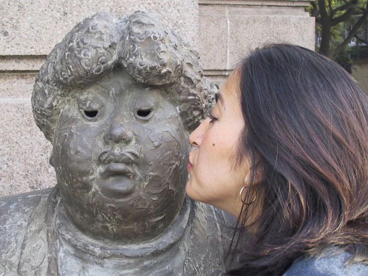 woman touching the face of a statue near a building