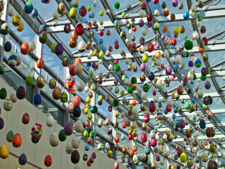 an array of colorful eggs are hanging from a ceiling