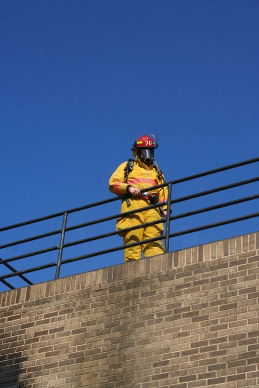 a man dressed in a yellow firefighter's uniform on top of a brick wall