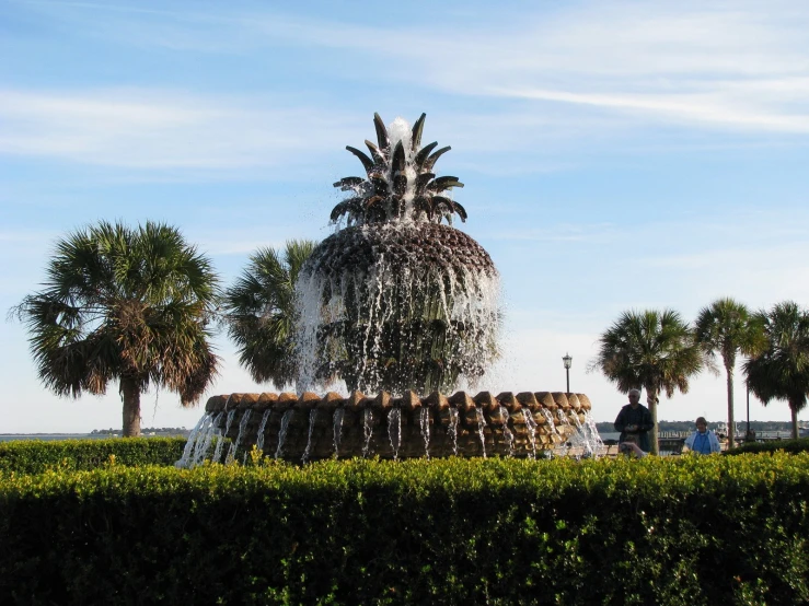 pineapple fountain on the side of a grassy area surrounded by trees