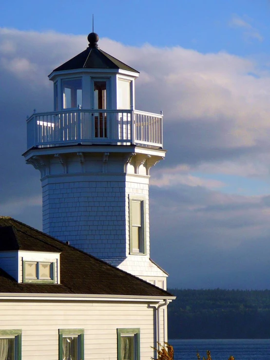 a light house stands near the ocean under a cloudy blue sky