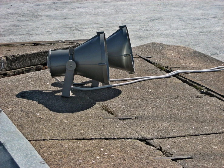 a silver speaker on the ground next to a pole