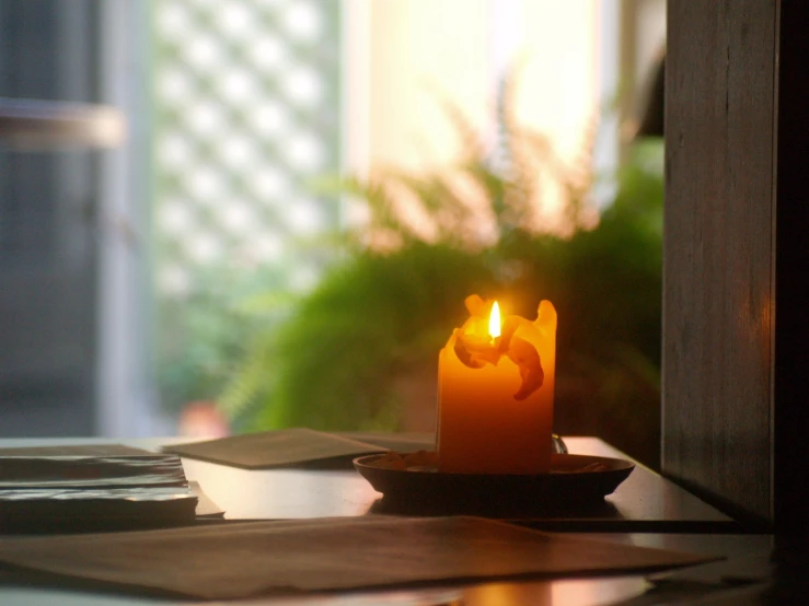 a candle is on top of a desk with papers and a window