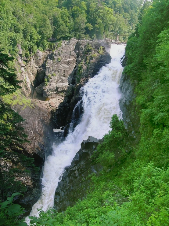 a waterfall running through green trees near a cliff