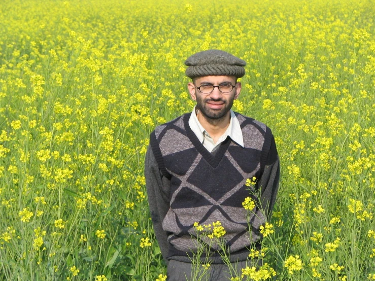 man in sweater standing in a field with yellow flowers