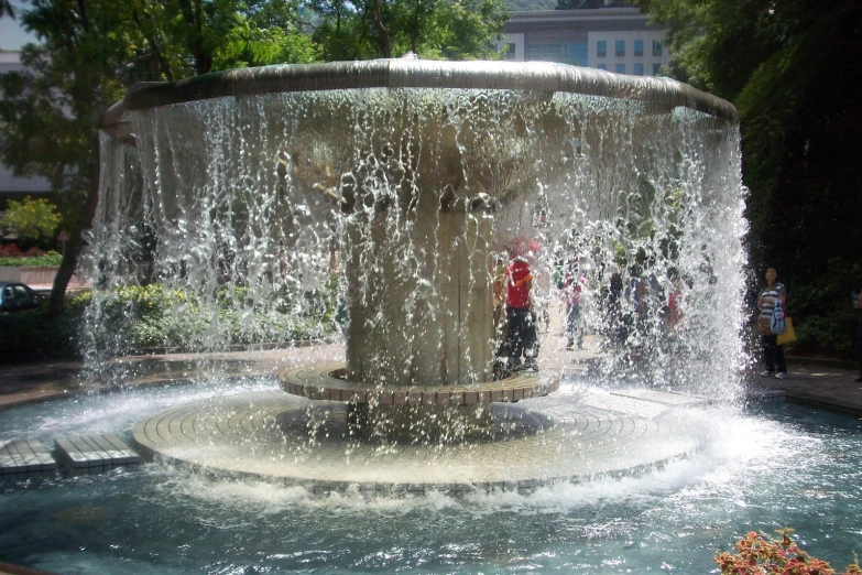 a fountain with water cascading around it, as people walk by on the sidewalk